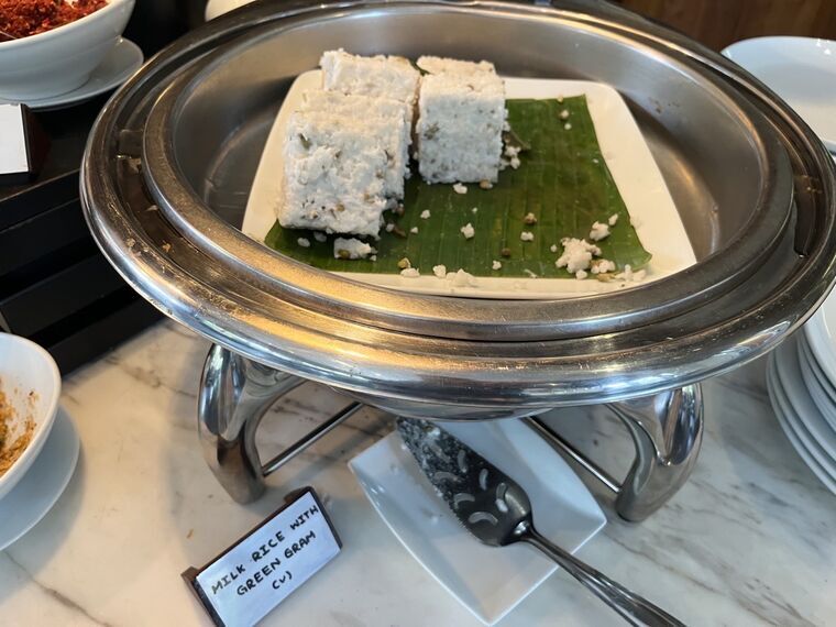 バナナの葉の上に切り分けられたキリバット4切れ。緑豆が混ざり、MILK RICE WITH GREEN GRAM (v)のプレートが手前に立つ