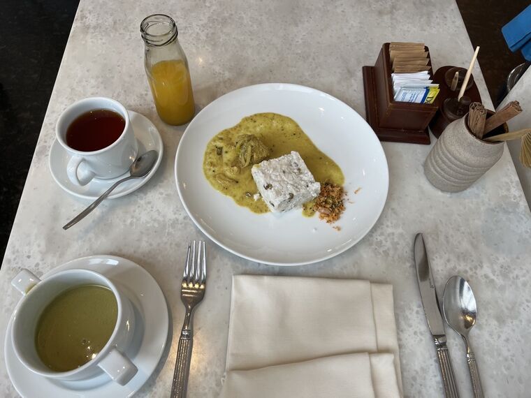 朝食のテーブル全景。白い皿に黄色いキリマールとキリバット、紅茶、パッションフルーツジュースの小瓶、コラキャンダのカップ、砂糖とシナモンスティックの木製ホルダー