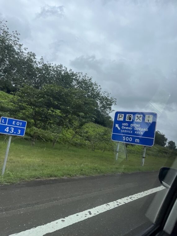 高速道路の青い標識。駐車・給油・レストラン・インフォメーションのピクトグラムとSERVICE AREA、500mの表示。左に距離標L E01 43.3