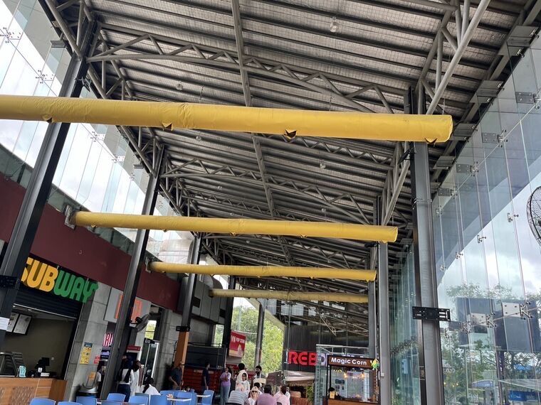 鉄骨がむき出しの高い天井に黄色いダクトが何本も走る。左下にSUBWAYの看板、奥にMagic Cornの屋台