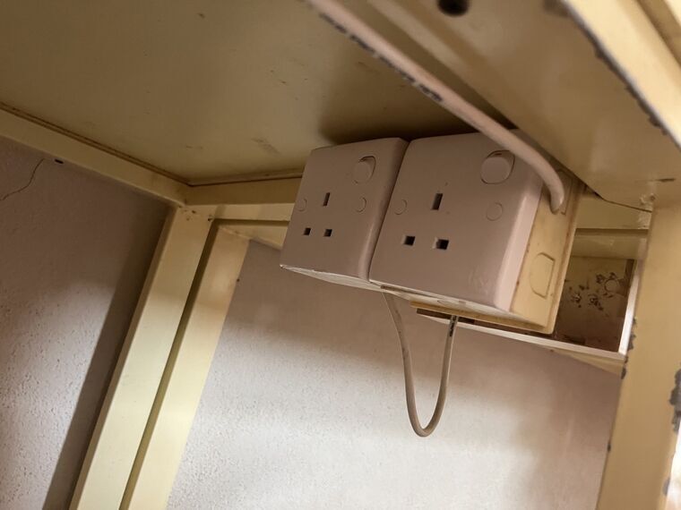 テーブルの裏側に取り付けられた白い電源タップ。イギリス式の3本ピン用の差込口が2口
