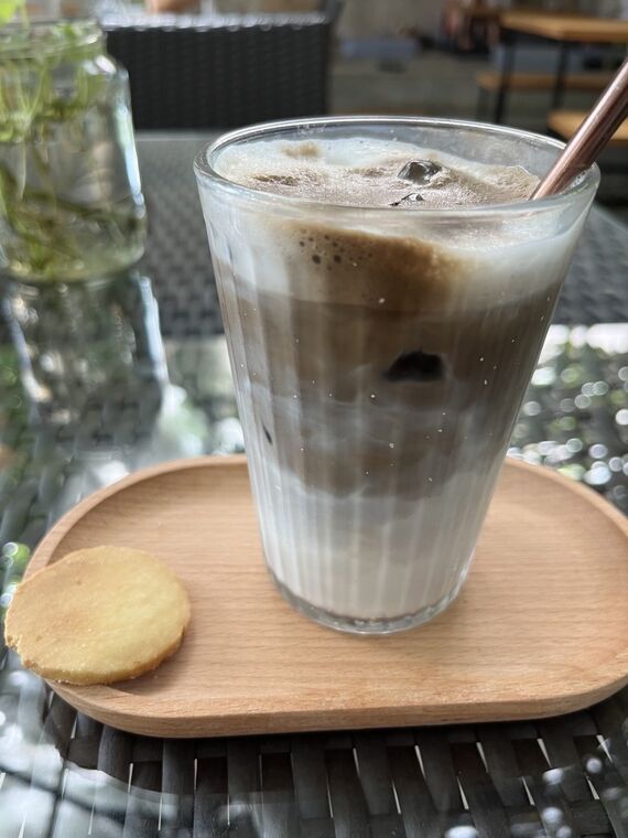 背の高いグラスに入ったアイスほうじ茶ラテ。ミルクと茶色い層が分かれている。木のトレイに丸いショートブレッドが添えられている