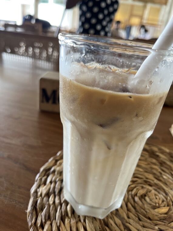 背の高いグラスに入ったアイスカフェラテ。下半分が白いミルクの層になっている。藁のコースターの上に置かれている
