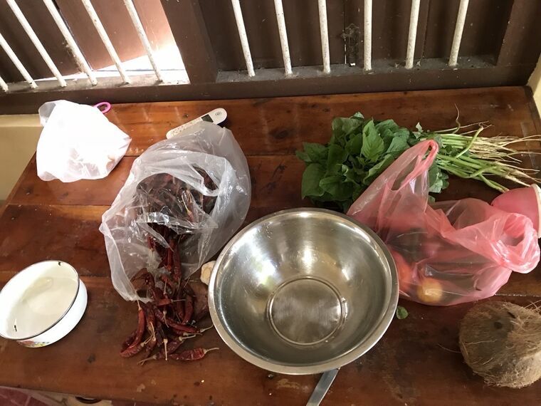 木のテーブルに並べられたkoolの食材。乾燥唐辛子、青菜の束、長ささげ、ステンレスボウル、皮付きのココナッツ
