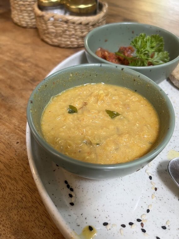 ミントグリーンの小鉢になみなみと入ったパリップ。豆の粒が残る濃いめの状態で、カレーリーフが2枚浮いている