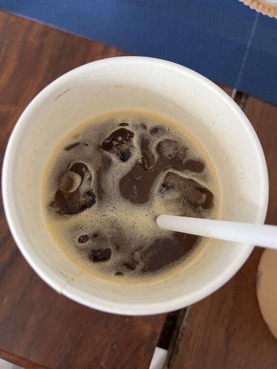 白いカップを真上から見たドリンク。表面は濃い茶色のコーヒーで、縁からオレンジ色が覗いている。白いストローが挿さっている