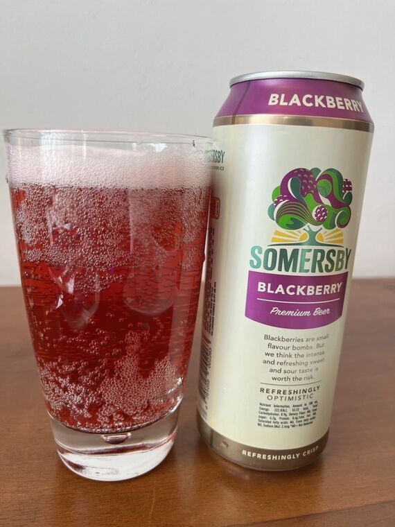 グラスに注いだSOMERSBY BLACKBERRY。液体は透き通った赤色で、グラスの側面に細かい泡が全面に張り付いている。右に紫のBLACKBERRY缶