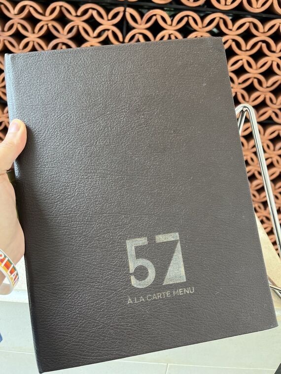 57 &Agrave; LA CARTE MENUと箔押しされた黒い革表紙のメニュー。背景はテラコッタの透かしブロックの壁