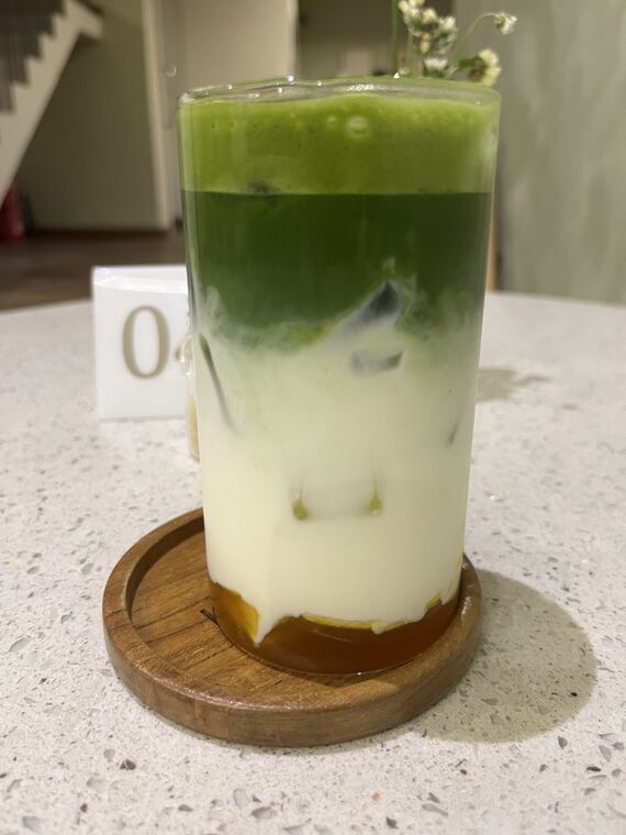 Mango Matchaを横から。上から抹茶の泡、濃い緑の抹茶、白いミルク、底にオレンジ色のマンゴーの層が分かれている