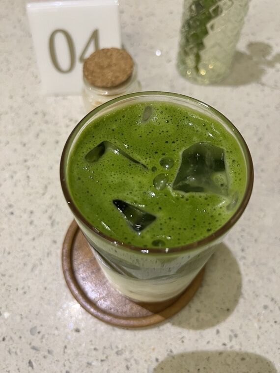 Mango Matchaを真上から。緑の泡と氷、奥に卓番04の札と砂糖のポット