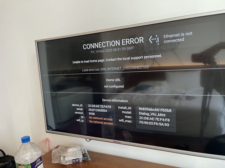 壁掛けテレビにCONNECTION ERROR、Ethernet is not connectedのエラー表示。画面下部にデバイス情報、手前のデスクに水のボトル