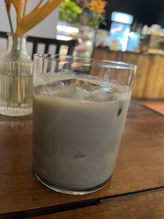 Black Cat Cafeのアイスのほうじ茶ラテ。リブガラスの花瓶と店内を背景に、氷の入ったベージュ色のラテ