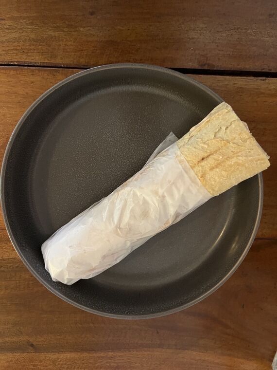 紙に包まれたSpicy Lamb Kofte Baguetteを黒い皿の上から。細長いバゲット