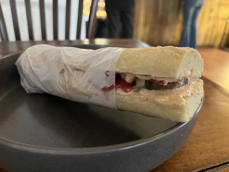Spicy Lamb Kofte Baguetteの断面。マトンコフタとビーツのピクルスオニオン、クリーム状のソース
