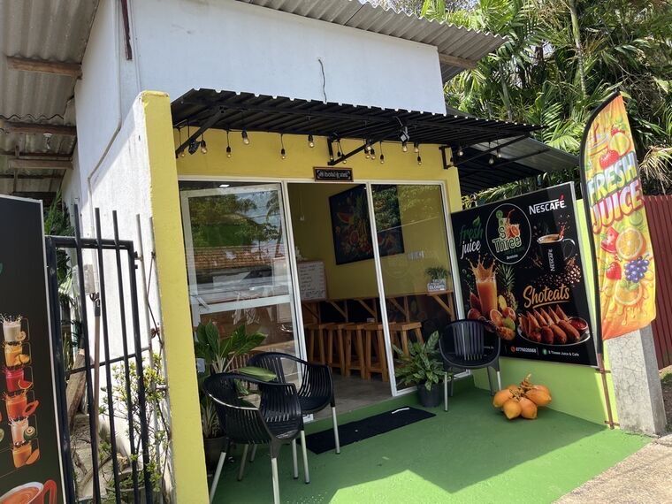 ベントータのS Three Juice &amp; Cafeの外観。黄色い壁の小さな店とFRESH JUICEののぼり、店先の黒いチェア