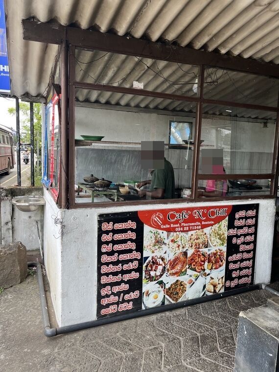 Cafe 'N' Chillの外観。トタン屋根のガラス張りキッチンで調理中のスタッフ。赤い看板にCafe` N' Chill、Galle Road, Phurumulla, Bentota、034 22 71546の表記とシンハラ語のメニュー一覧