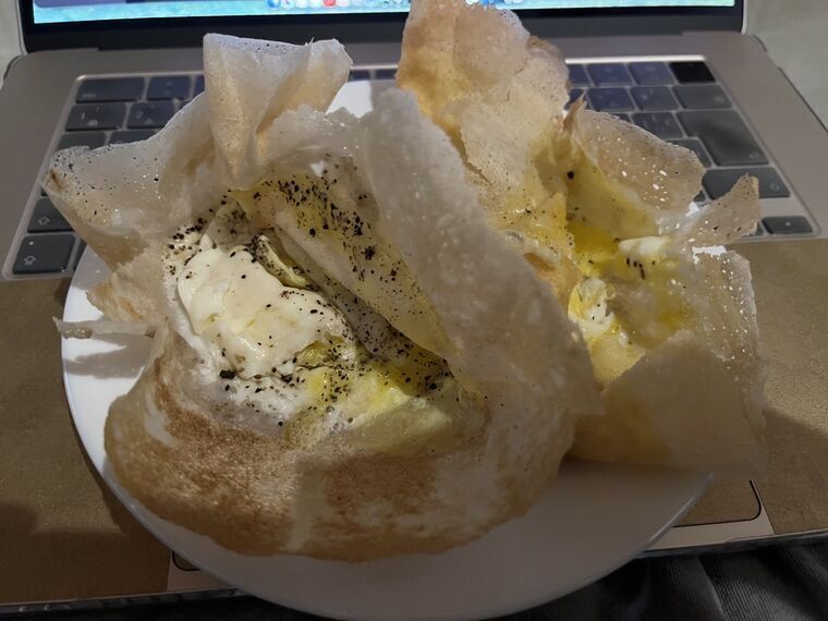 持ち帰ったビッタラアーッパ2個。白い皿の上で、薄くパリッとした生地の中に目玉焼きと黒こしょう