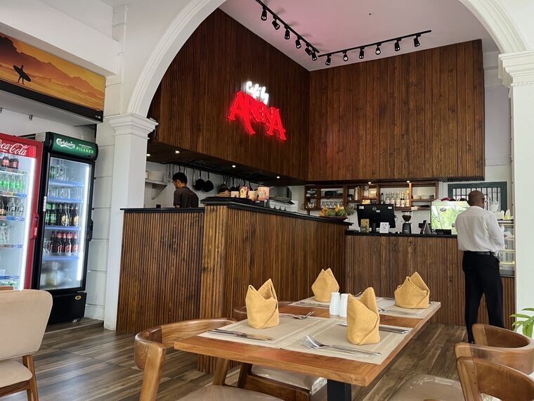 Cafe by arenaの店内カウンター。赤いARENAのネオンロゴ、木目調の内装、飲料冷蔵庫