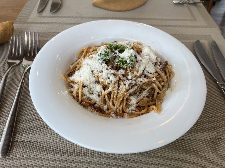スパゲッティボロネーゼ。パルメザンチーズと刻んだパセリがトッピングされた白い深皿