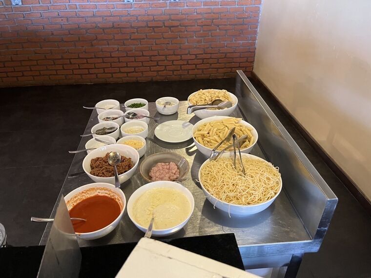 パスタステーションの具材。マカロニやペンネ、ミートソース、チーズ、薬味の小鉢が並ぶ