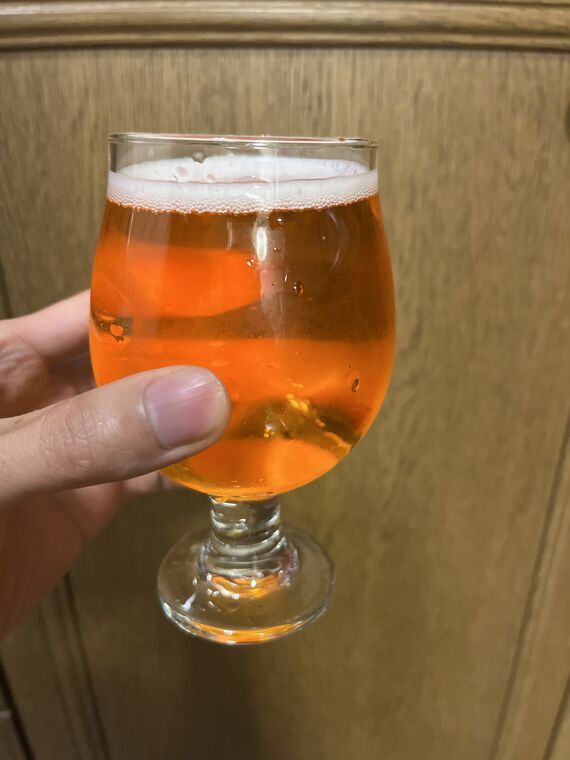 小ぶりのステムグラスに注いだSOMERSBY MANGO & LIMEを手に持ったところ。液体はオレンジがかった赤色