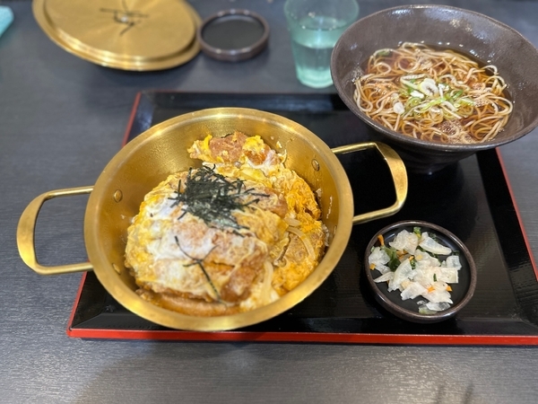 鍋の蓋を開けてかけそばにネギを入れて漬物来た