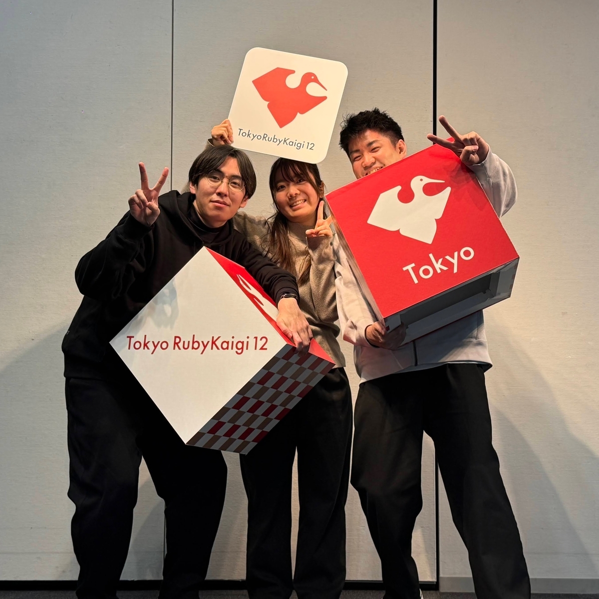 東京Ruby会議12のロゴ入り小道具を持った3人が、フォトスポットで笑顔でポーズを取っている