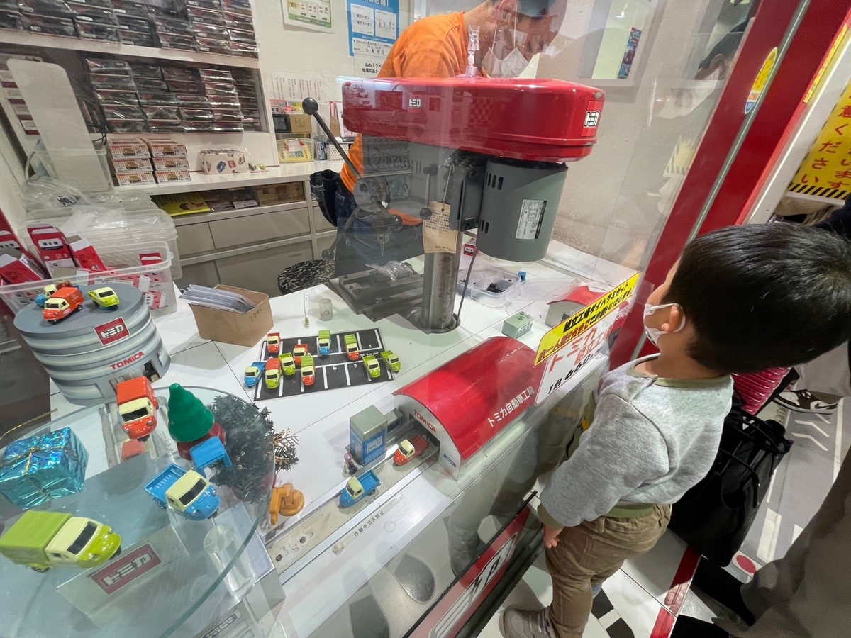 東京駅の東京一番街・東京キャラクターストリート「トミカショップ」にあるトミカ組み立て工場の作業を見ている男児