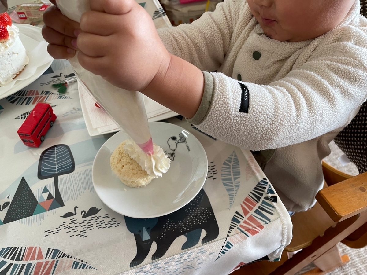 手づくりのクリスマスケーキに生クリームを絞る男児