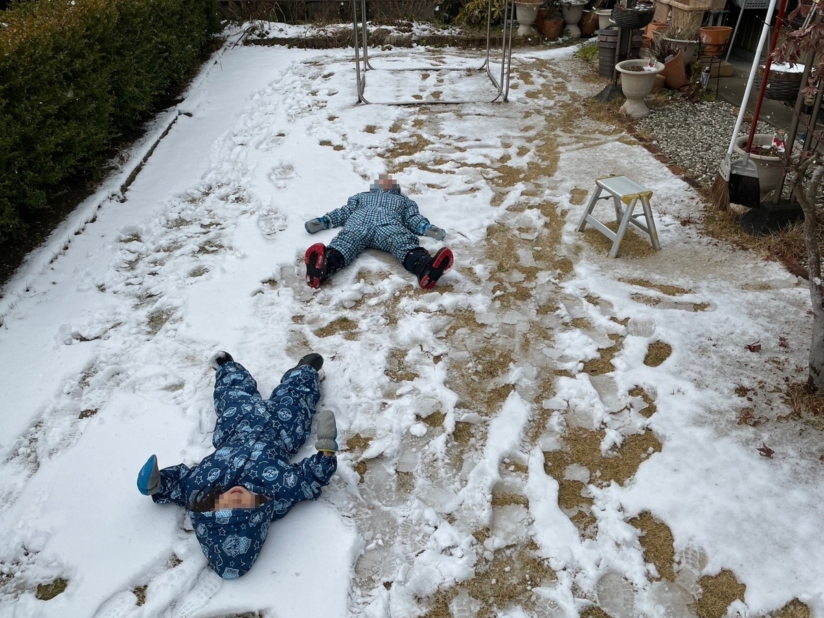 庭で雪の上に寝そべる兄妹