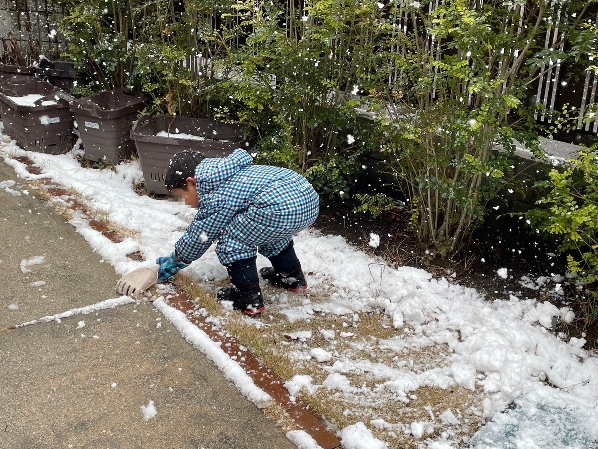 庭で雪かきをする男児