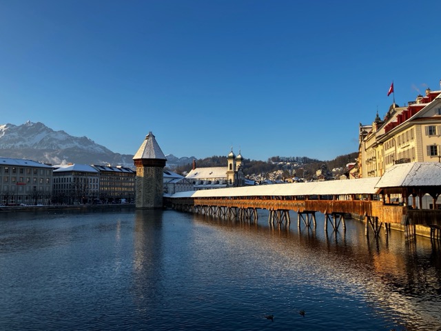 雪化粧をしたスイス・ルツェルンのカペル橋。背景には冬のアルプス山脈が広がる景色