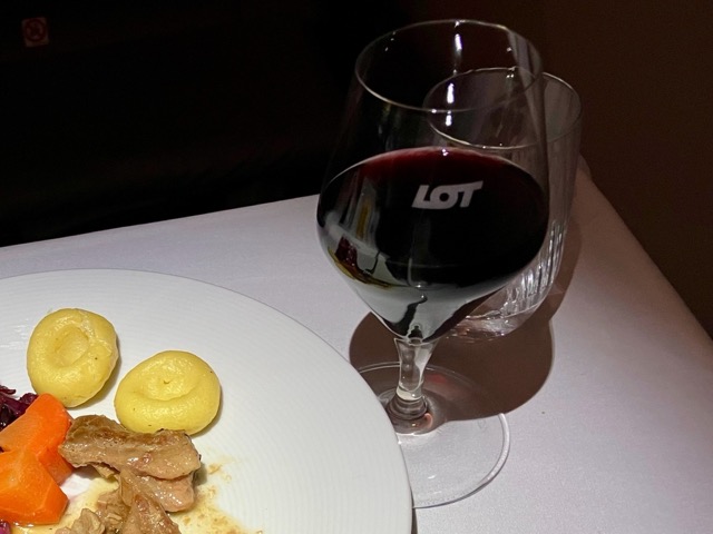 LOTのロゴが入ったグラスに注がれた赤ワイン。横には機内食のメインディッシュ