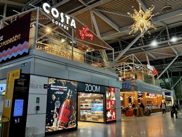 ワルシャワ空港ターミナル内の店舗エリア。2階のコスタコーヒーと、1階のZOOMショップ、大きなデジタル広告