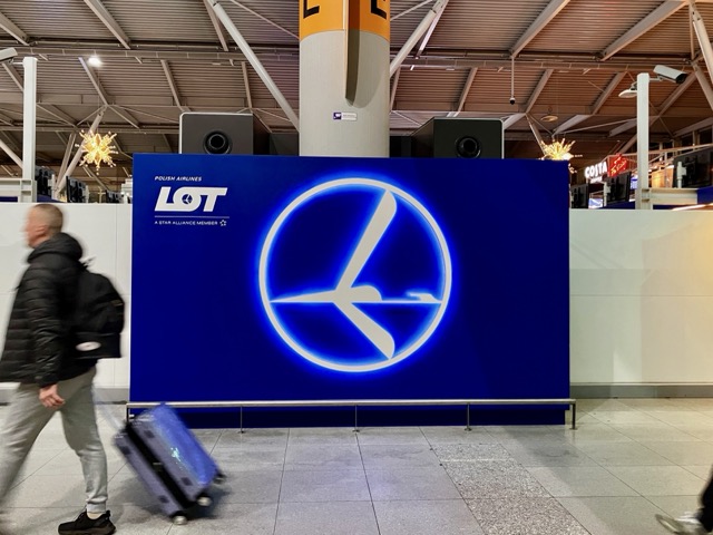 ワルシャワ空港に設置されたLOTポーランド航空の大きな点灯ロゴ。手前を旅客が通り過ぎている
