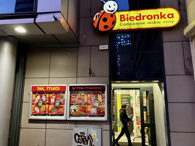 Biedronka（ビエドロンカ）の入り口。今週のセール情報が掲載された赤いチラシと、入店する客の様子