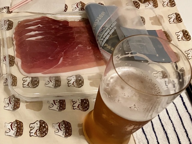 グラスに注がれたビールと、パック入りの生ハム。部屋でくつろぎながら楽しむ晩酌の様子