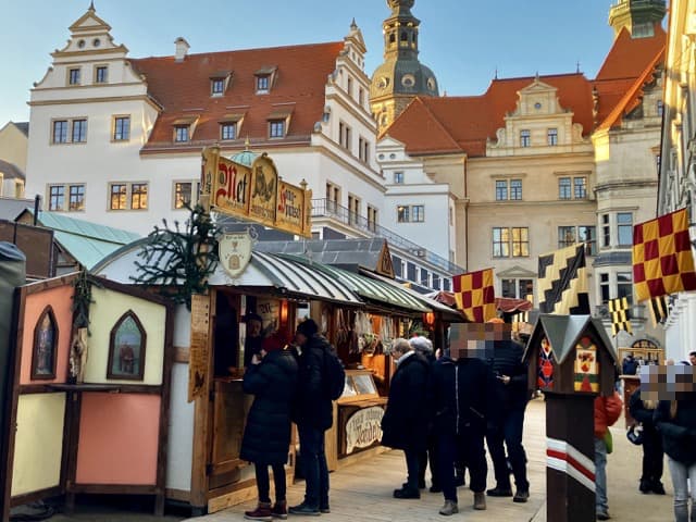 ドレスデン城内のシュタールホーフ（Stallhof）で開催されている中世風クリスマスマーケット。歴史的な建物と紋章の旗、木造の屋台が並ぶ情緒ある風景