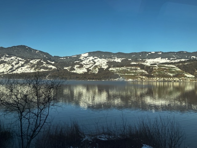 鉄道の車窓から撮影した、鏡のような湖面に逆さに映るスイスの雪山