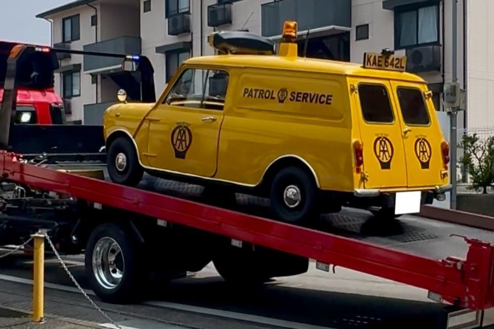 Classic Mini AA van being loaded onto red transport truck in garage
