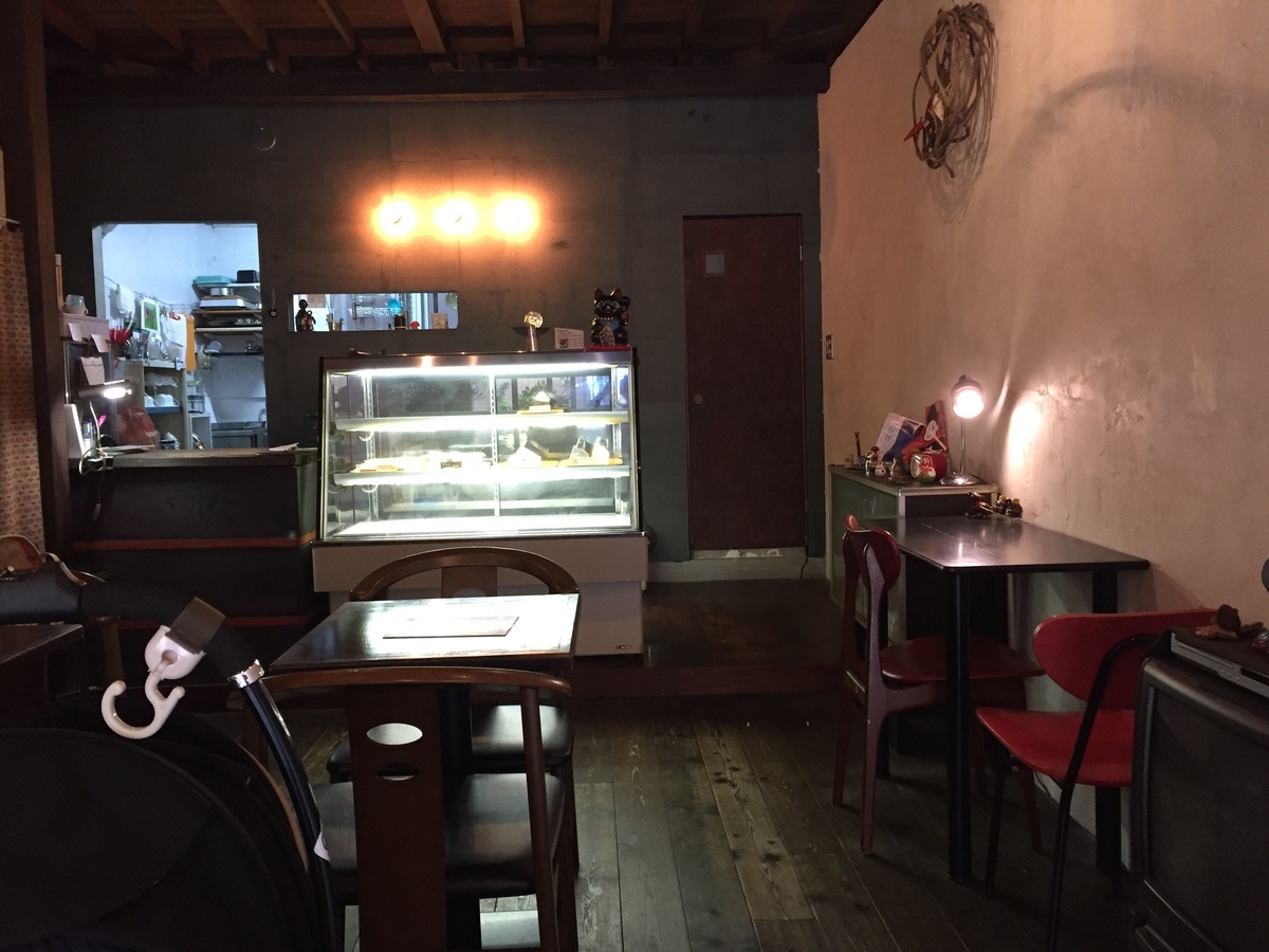 店内を入り口側から撮っている。テーブル席があり、奥にはケーキのショーケースとレジ、さらに奥にはキッチンが見える