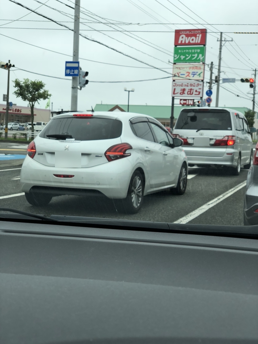 車の助手席から正面を撮った写真。赤信号やロードサイド店舗の看板、他の車両などが写っている。