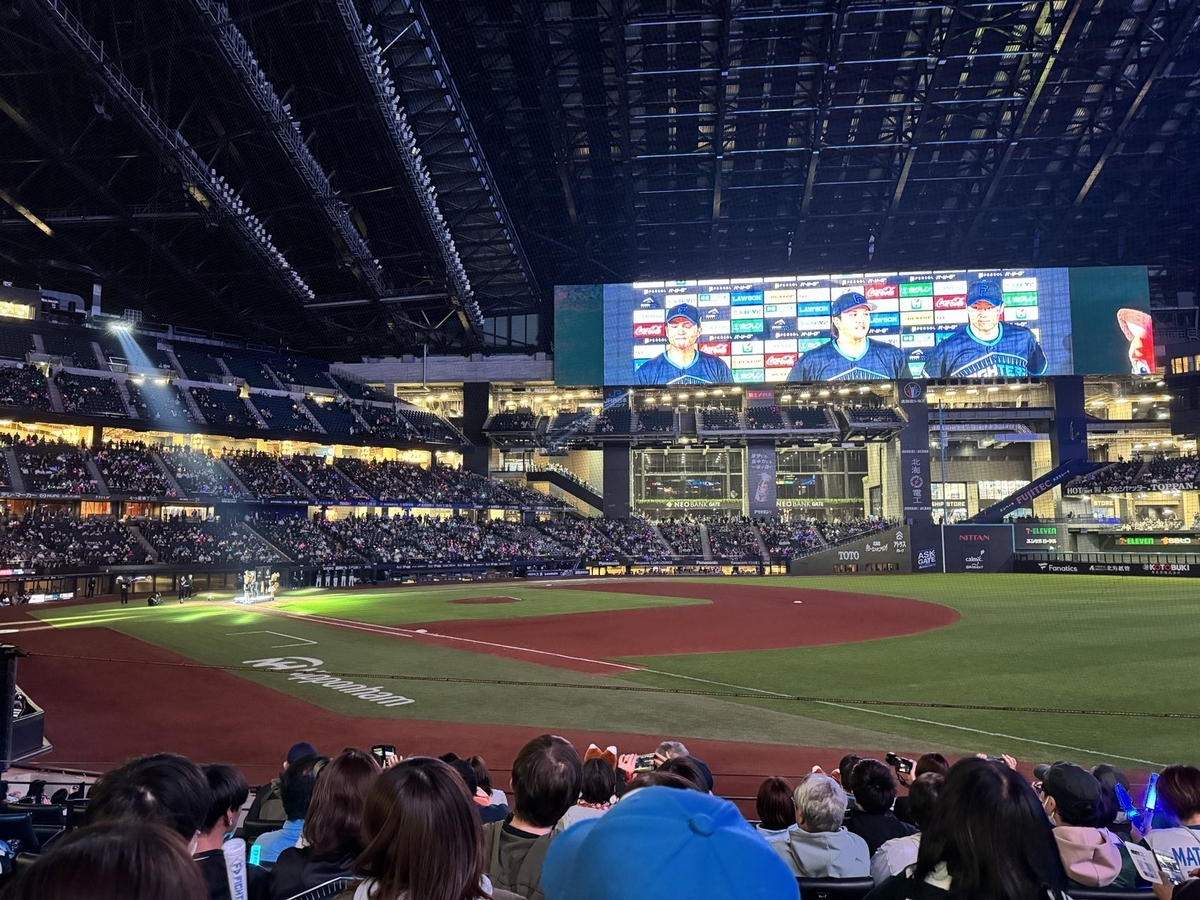 北海道日本ハムファイターズ 本拠地のエスコンフィールド北海道 1塁側内野席からの写真。試合後のヒーローインタビュー中。正面の大型LEDビジョンには、本日のヒーローである3人が映し出されている。左から郡司 裕也（ホームランで逆転した内野手）・伏見 寅威（千歳市出身の捕手。攻守ともに活躍。）・山﨑 福也（先発ピッチャー。7回1失点の大健闘）