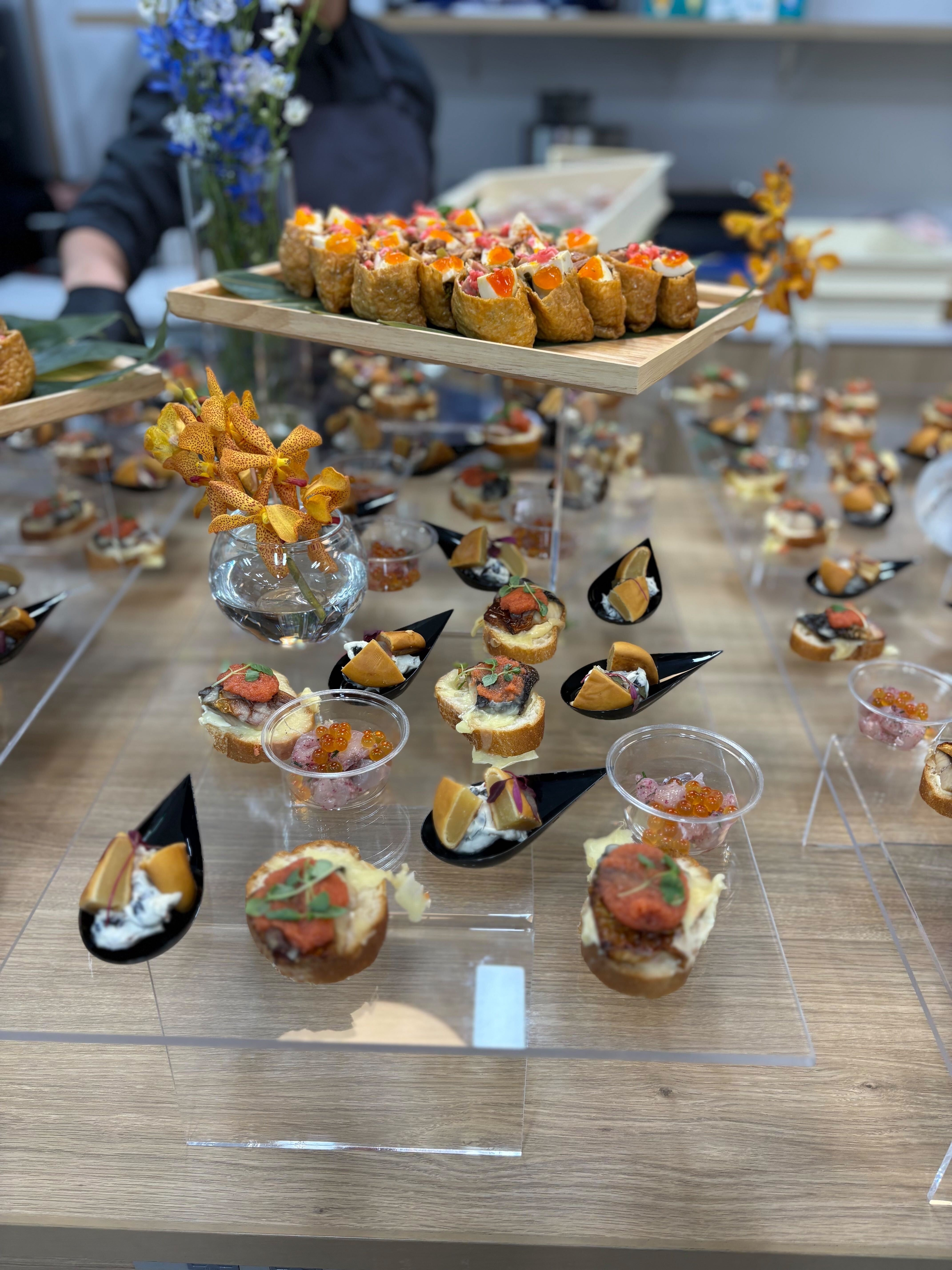料理のアップの写真。一口でつまめるような料理が色鮮やかにテーブルを彩っているだけでなく、各企業をイメージした青や白、オレンジなどの花も添えられている。