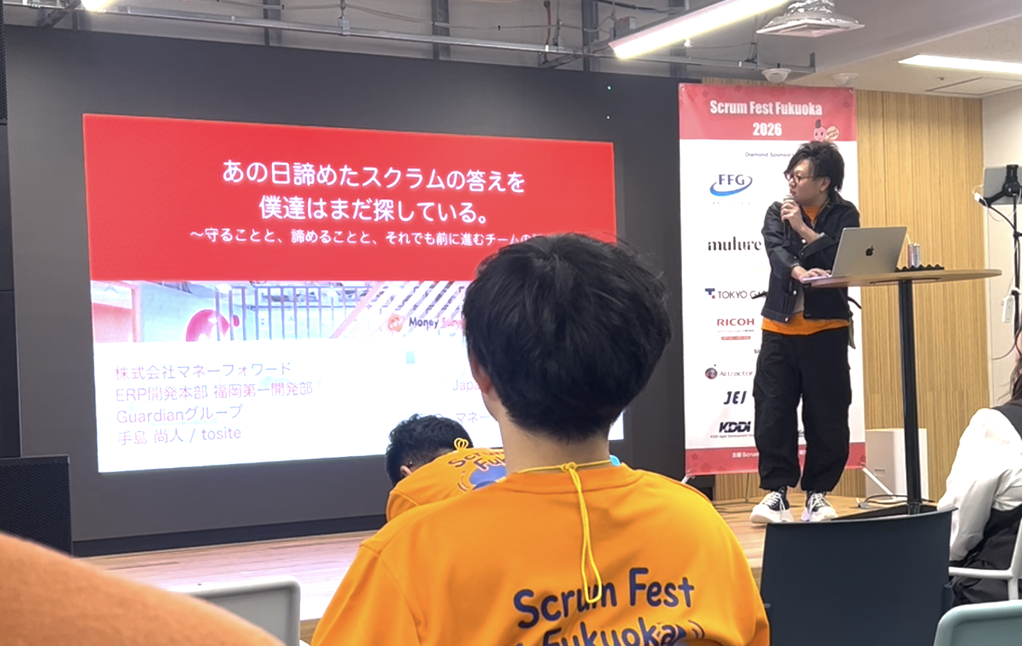 登壇者の手島さんがマイクを持って喋っている写真。