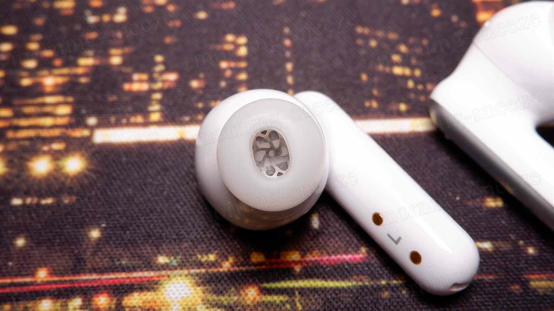 白色のイヤホンのアップ画像。左側にはイヤーカップ、中央にはメッシュ状のスピーカー部分が見える。