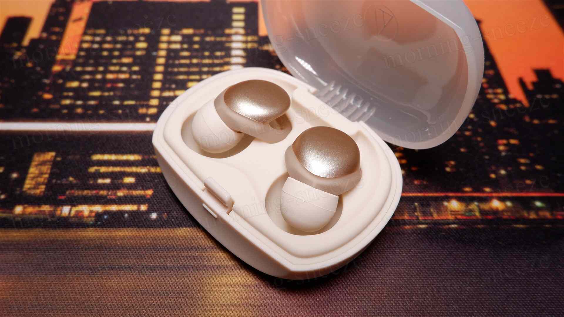 白いケースに収められた二つの金色のイヤホンが置かれています。