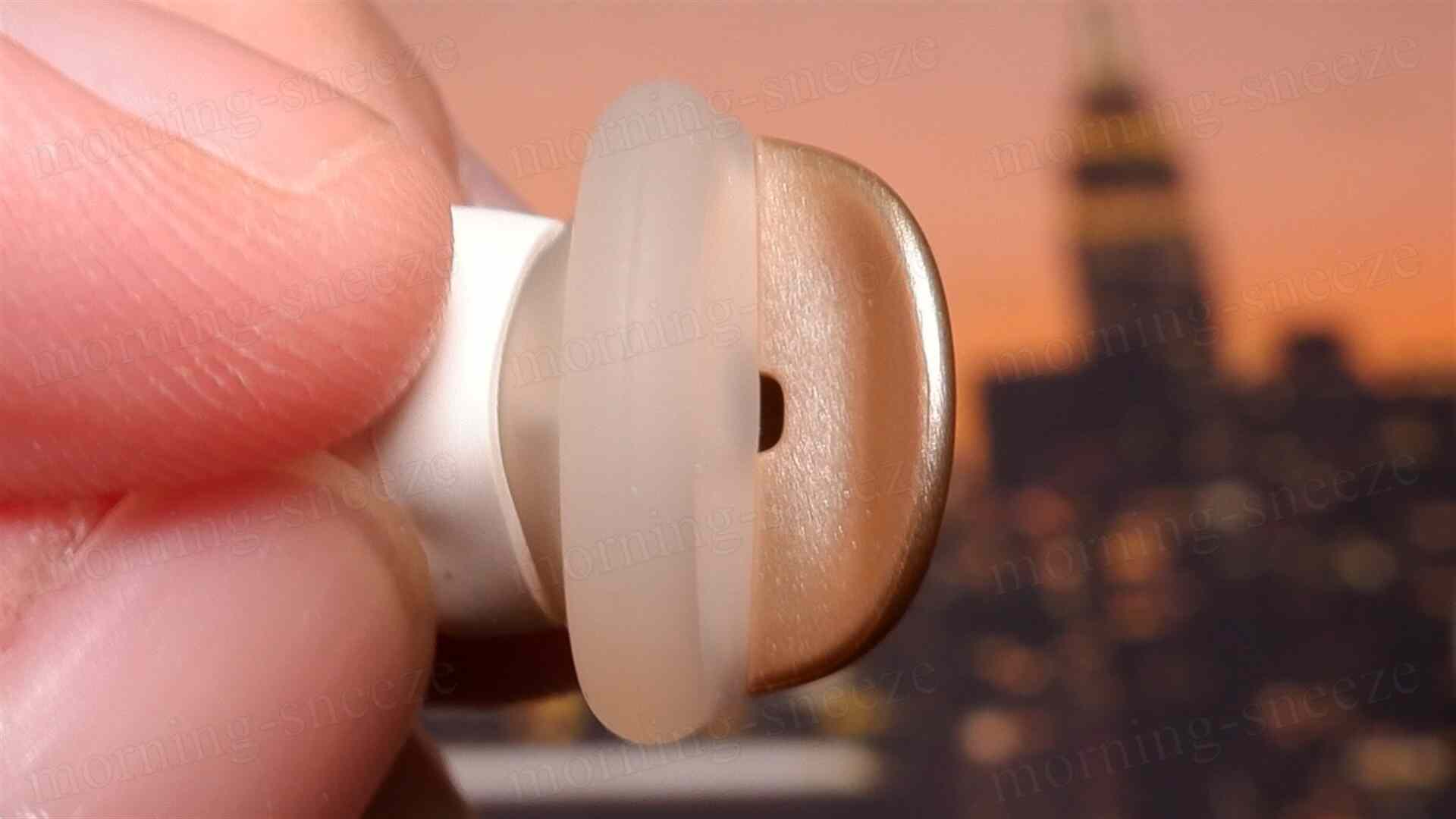 指で持たれた耳栓のシェル拡大図。ボディは金色で、内側中央部にピンホールが付いている。