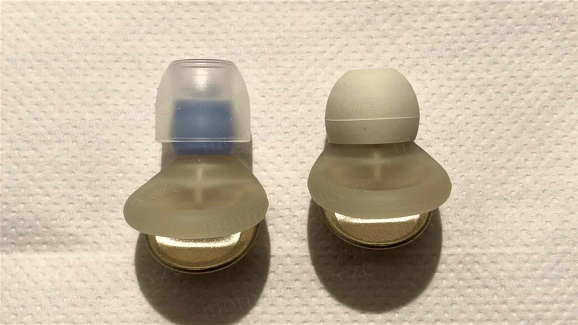 耳栓が2つ並んでいる画像。左側は透明の上部と青色のアクセントがあるデザイン、右側は白色の上部を持つシンプルなデザイン。どちらもソフトな素材で作られている。背景は白い紙タオル。