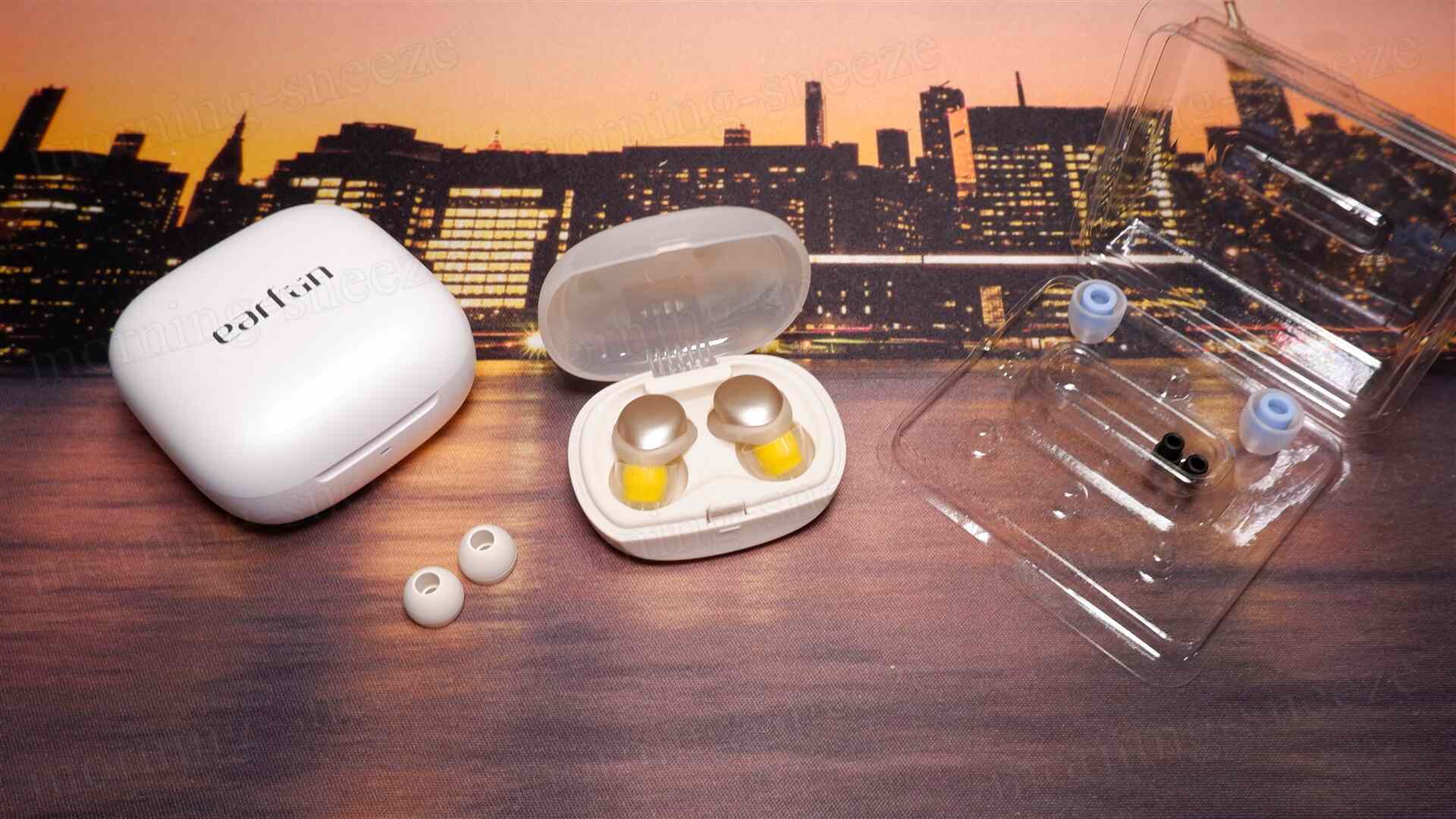 イヤープラグが入った白いケース、オープンの状態でイヤープラグが見えている。右には透明な箱に収められたイヤーチップあり、色とりどりのイヤーチップが2つ並んでいる。背景には夜景が広がっている。